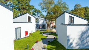 Un bâtiment moderne, de couleur blanche, avec un chemin pavé et de petits parterres de fleurs.