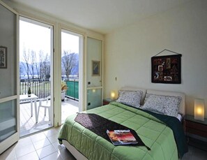 A bedroom with a bed, a balcony, a painting, and a window.