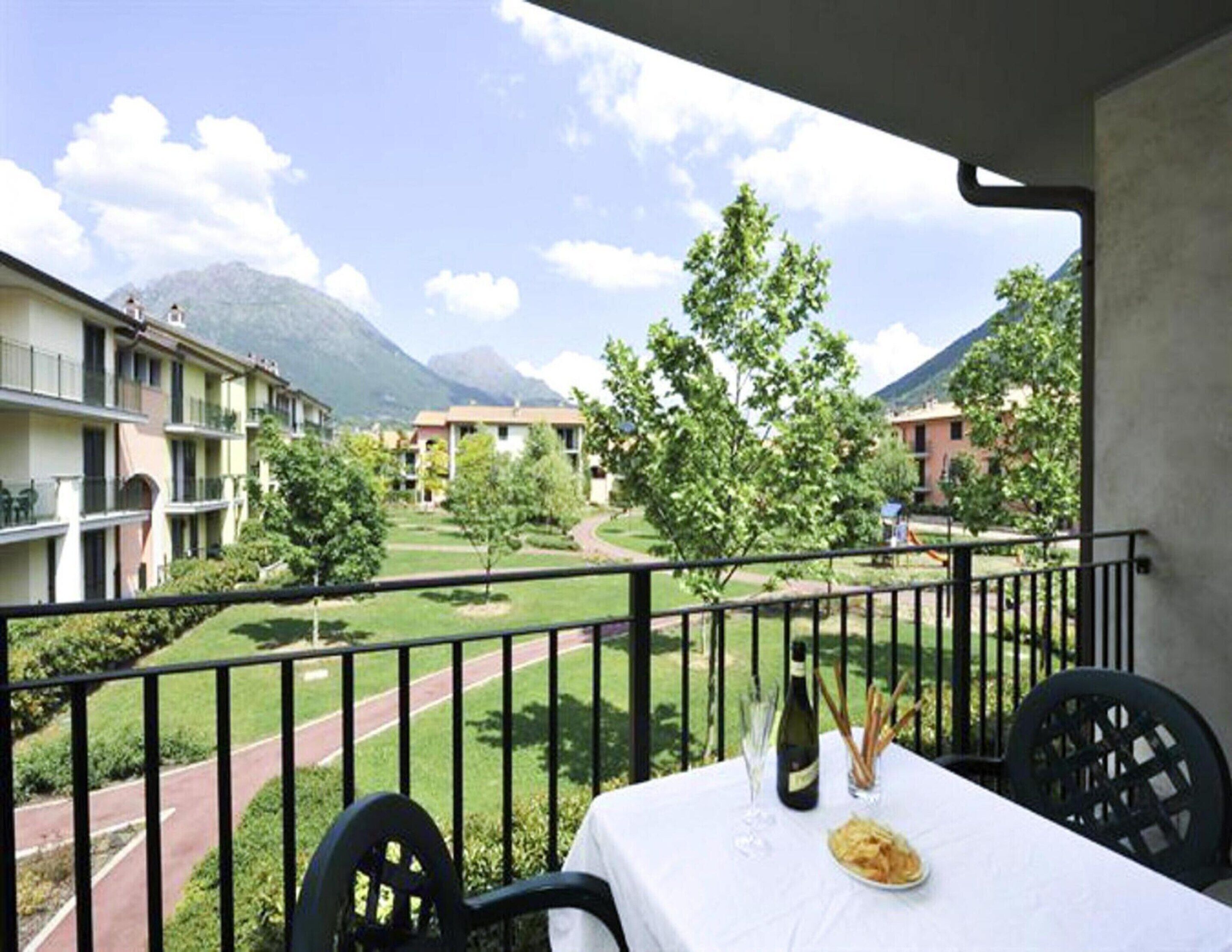 A balcony with a table set for dining, overlooking a courtyard with buildings and trees, and a mountain in the background.