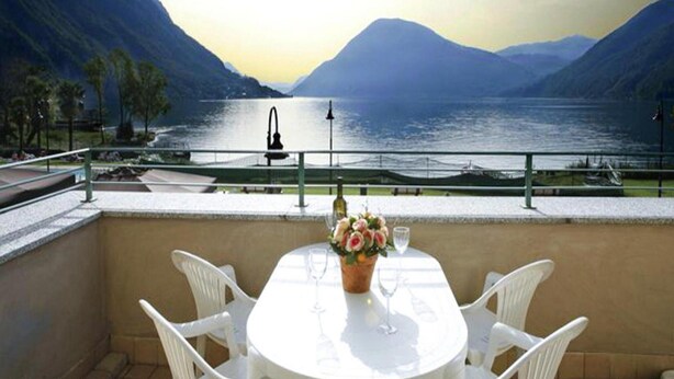 A terrace with a table and chairs overlooking a lake with mountains in the background. - Apartment in Porlezza With Lake View (Porlezza)