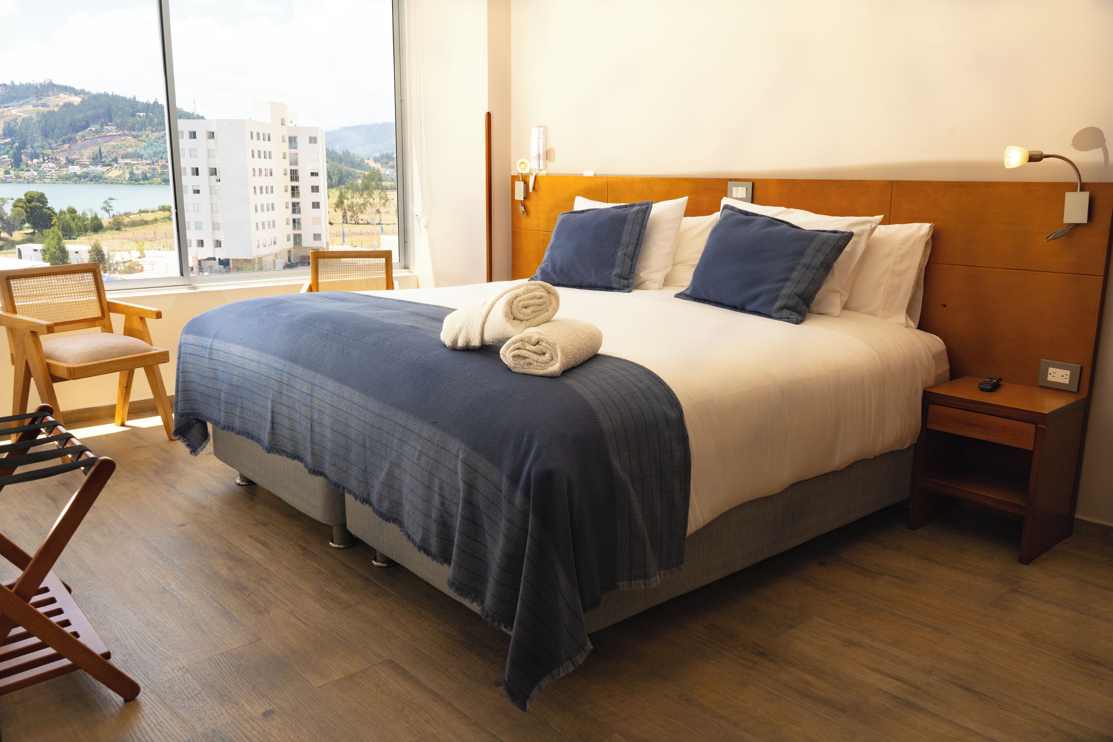 Habitación de hotel con una cama grande, cabecero de madera y vistas a un cuerpo de agua y edificios.