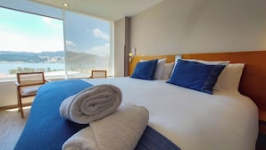 Une chambre d’hôtel avec un grand lit, une vue sur la mer et un fauteuil près de la fenêtre.