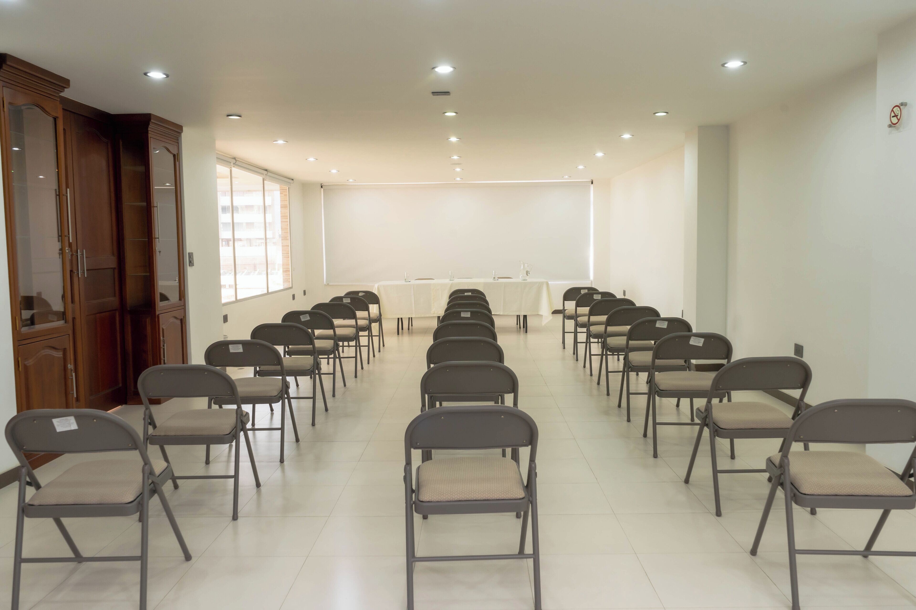 A conference room with rows of foldable chairs, a large projection screen, and wooden cabinets.