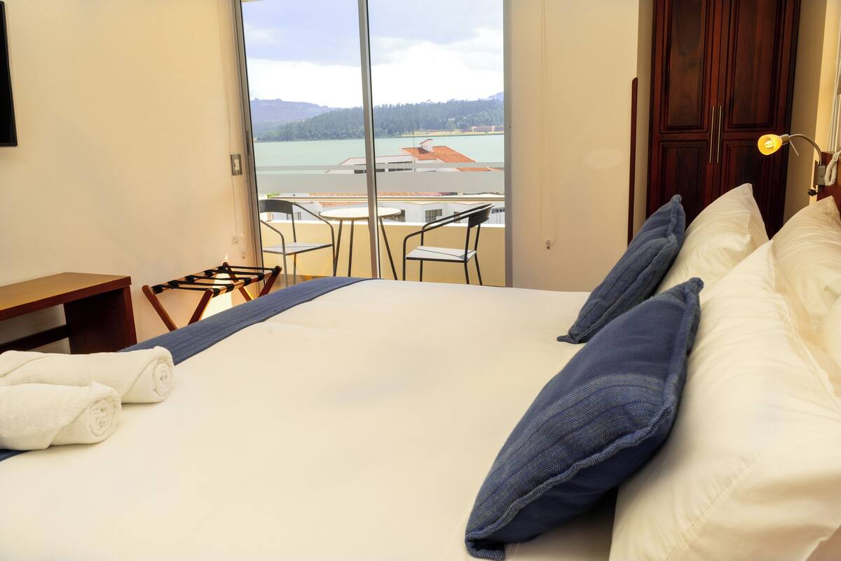 A hotel room with a bed, a desk, a chair, and a view of a body of water and buildings.