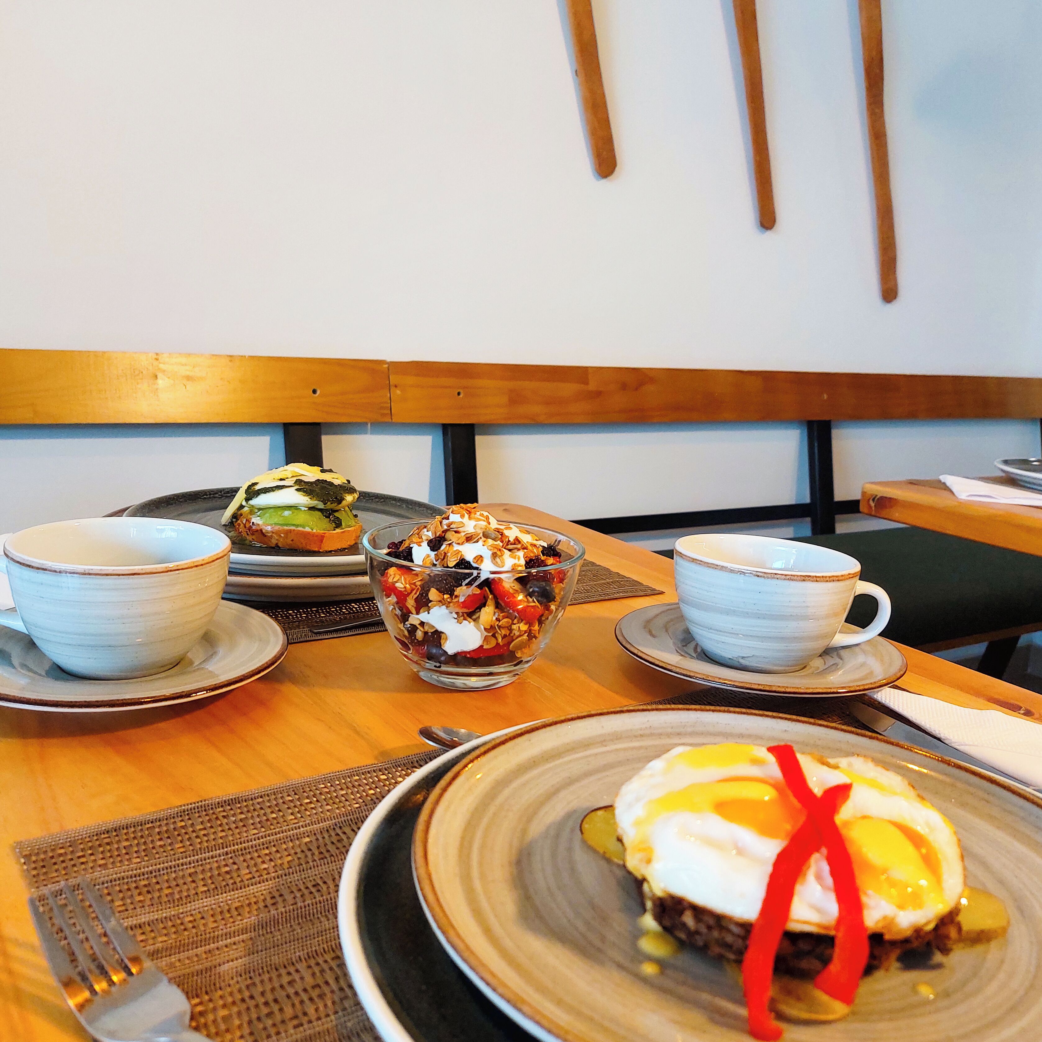 Une table à manger avec une assiette d’œufs Bénédicte, un bol de granola et deux tasses de café.