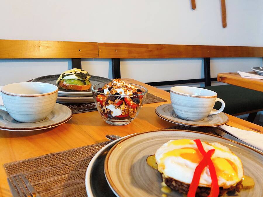 Une table à manger avec une assiette d’œufs Bénédicte, un bol de granola et deux tasses de café.