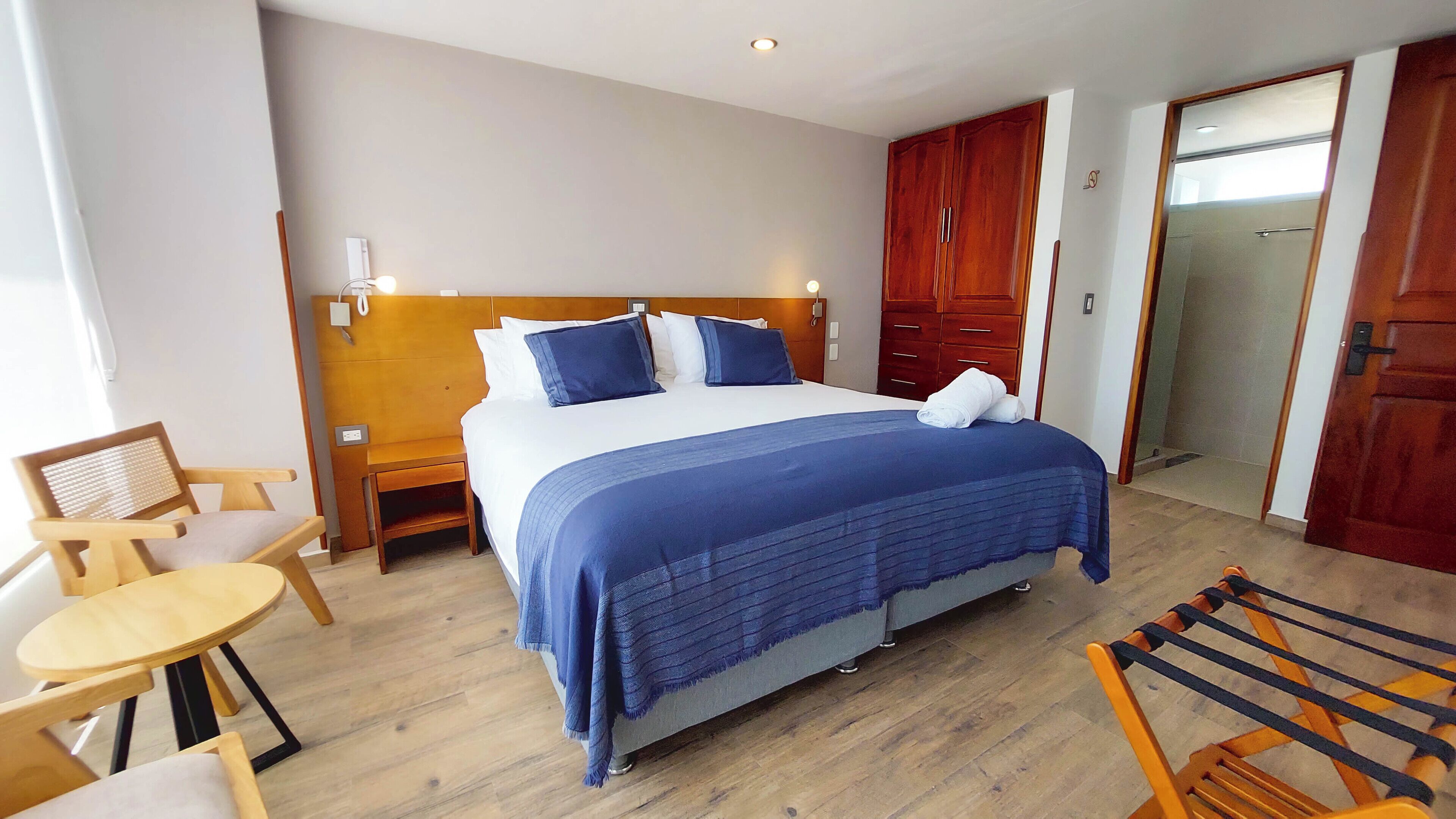 Une chambre d’hôtel comprenant un lit, des tables de chevet en bois, une chaise, une petite table et une armoire.