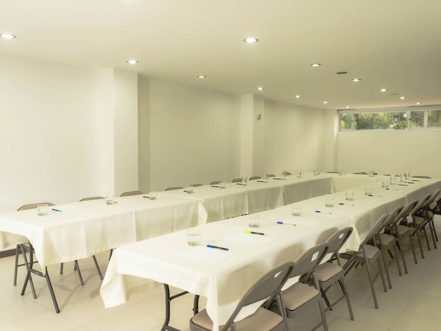 Un salón de conferencias con mesas largas, sillas y un ventanal con vistas a árboles.