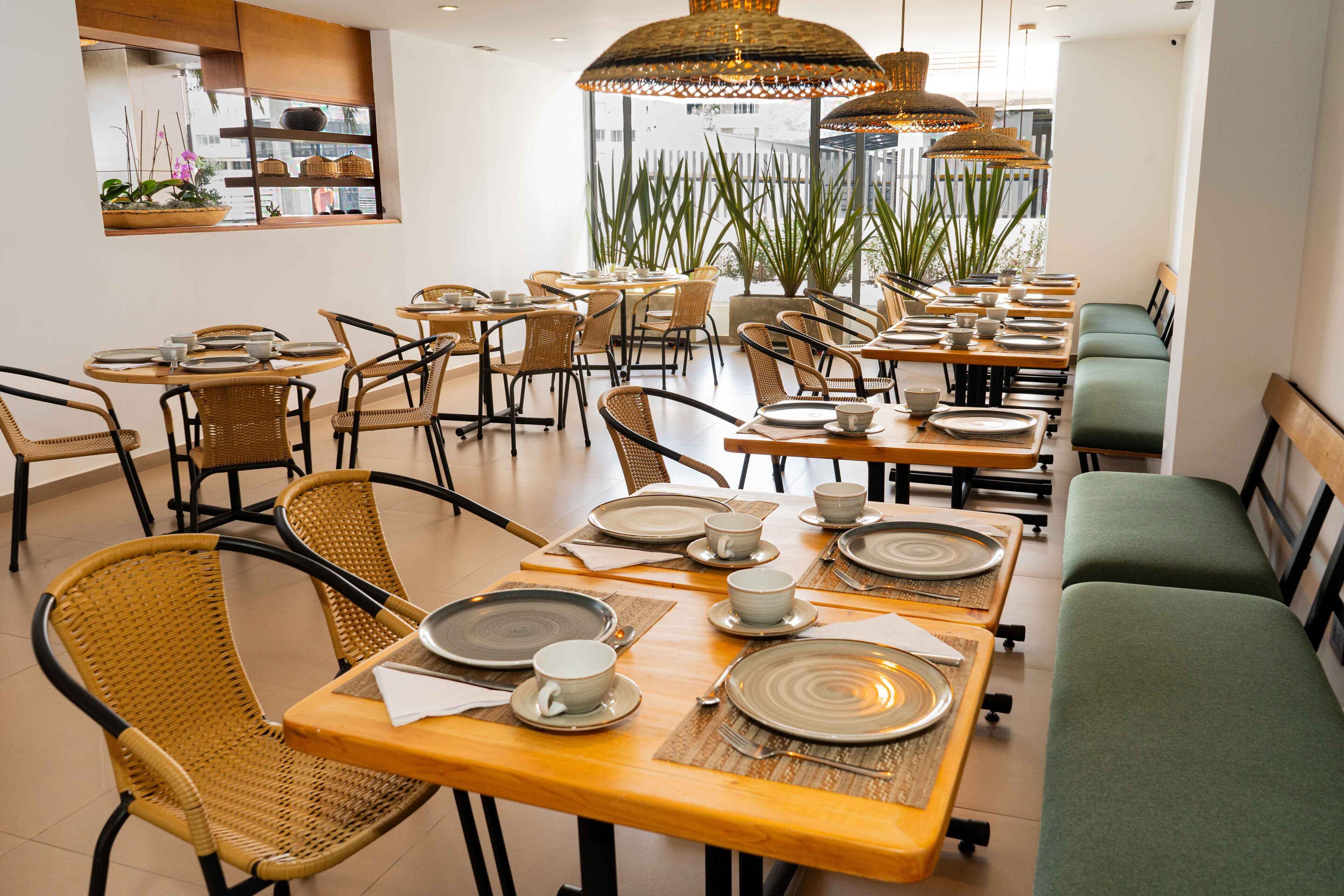 A restaurant with multiple tables set for dining, wicker chairs, and hanging wicker lamps.