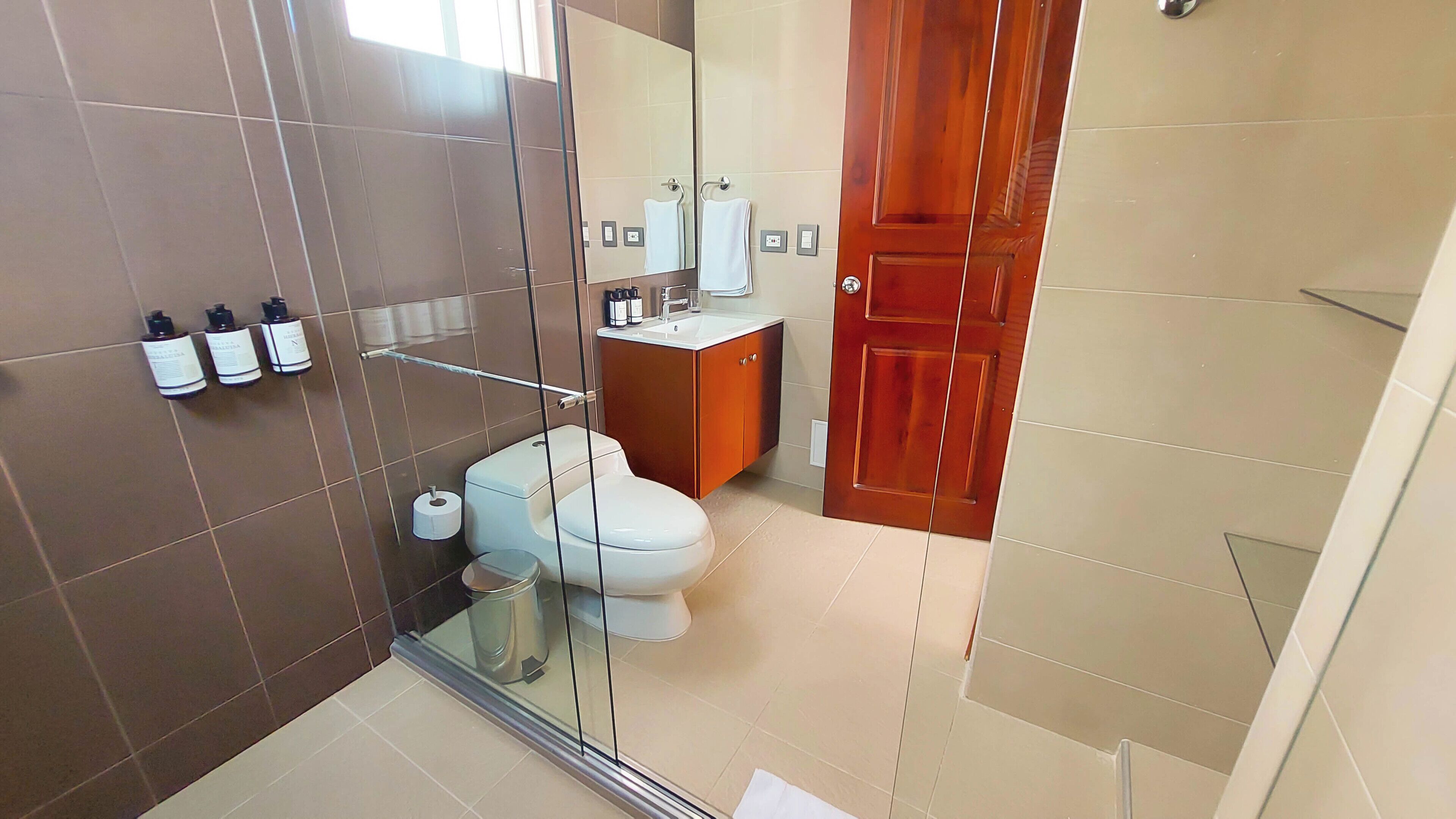 Un baño moderno con cabina de ducha de vidrio, un inodoro, un lavabo con espejo y un armario de madera.