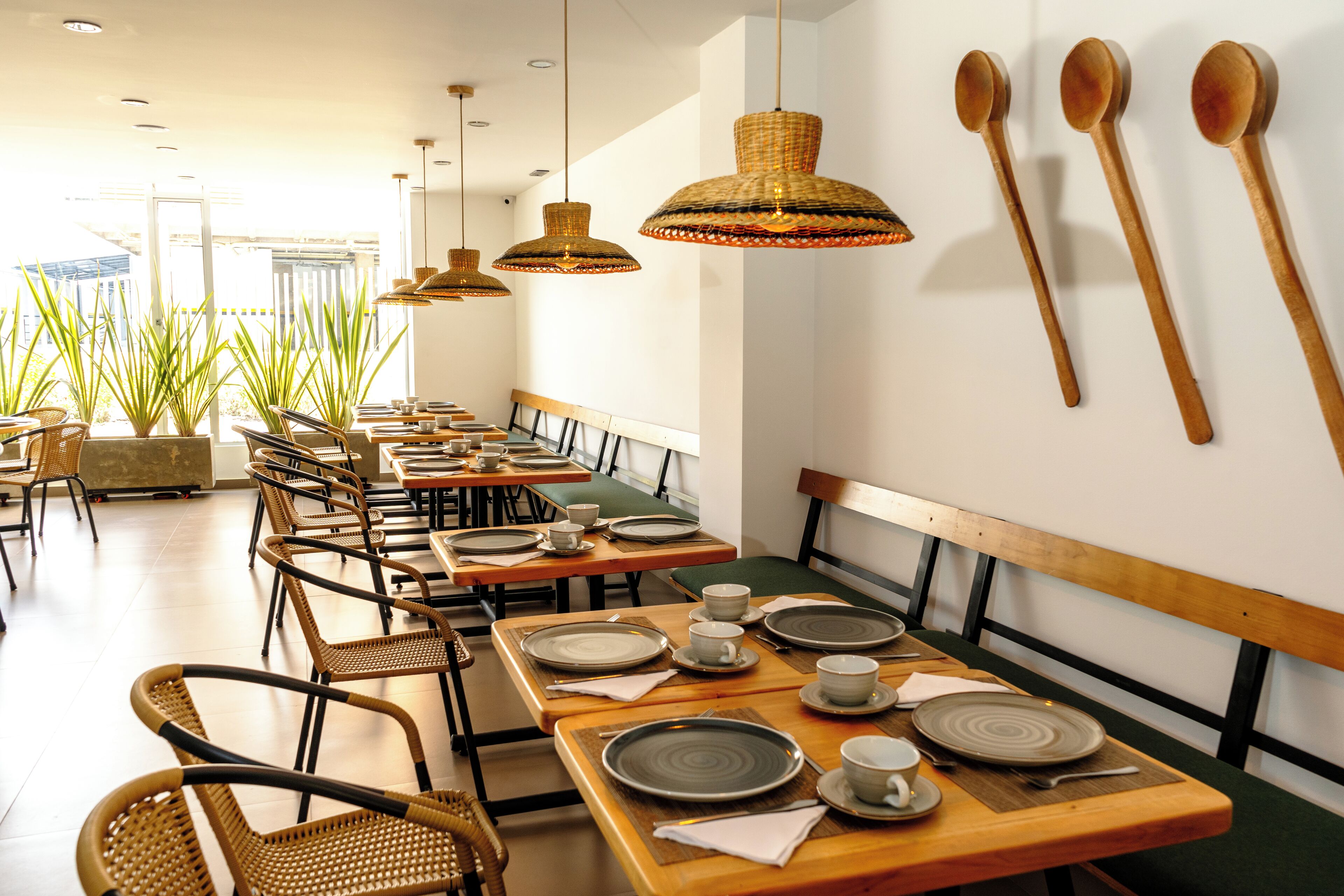 A restaurant with wooden tables and chairs, hanging wooden spoons, and large woven pendant lights.