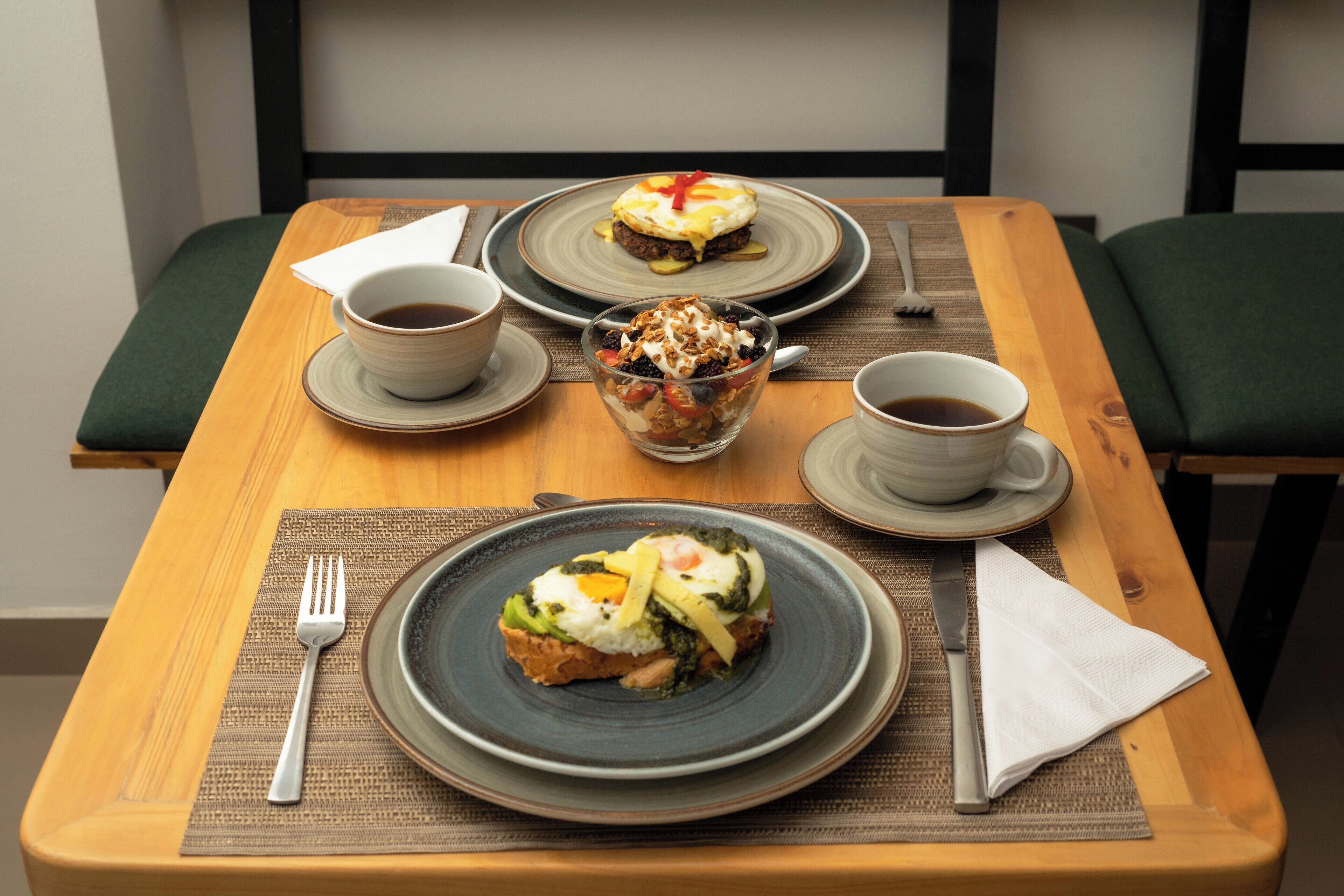 A dining table with two plates of food, a bowl of dessert, and two cups of coffee.