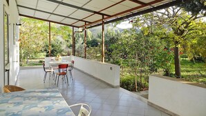 A covered patio with a table and chairs, surrounded by greenery and trees. - Holiday Home, Solanas (Sinnai)