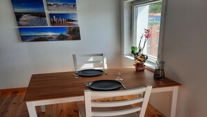 A dining area with a wooden table and white chairs, a window with a view, and three framed pictures on the wall. - Charmante Ferienwohnung in der Oase am Vilzsee (Mirow)