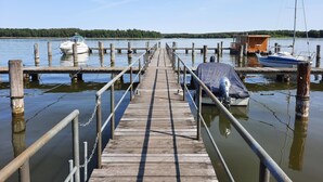 A wooden pier extending into calm water, with boats docked at both ends and a small wooden structure on the right. - Charmante Ferienwohnung in der Oase am Vilzsee (Mirow)