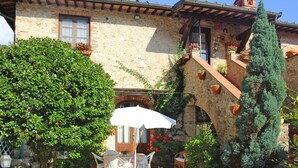 Un bâtiment en pierre doté d’un patio comprenant une table et des chaises, le tout abrité par un parasol blanc.