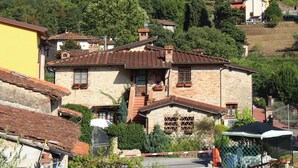 Un bâtiment traditionnel en pierre, doté d’un toit en tuiles, entouré de verdure et d’autres constructions.