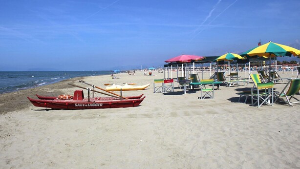 Une plage bordée de rangées de chaises de plage et de parasols, avec un poste de surveillance pour les sauveteurs et une rangée de bateaux.