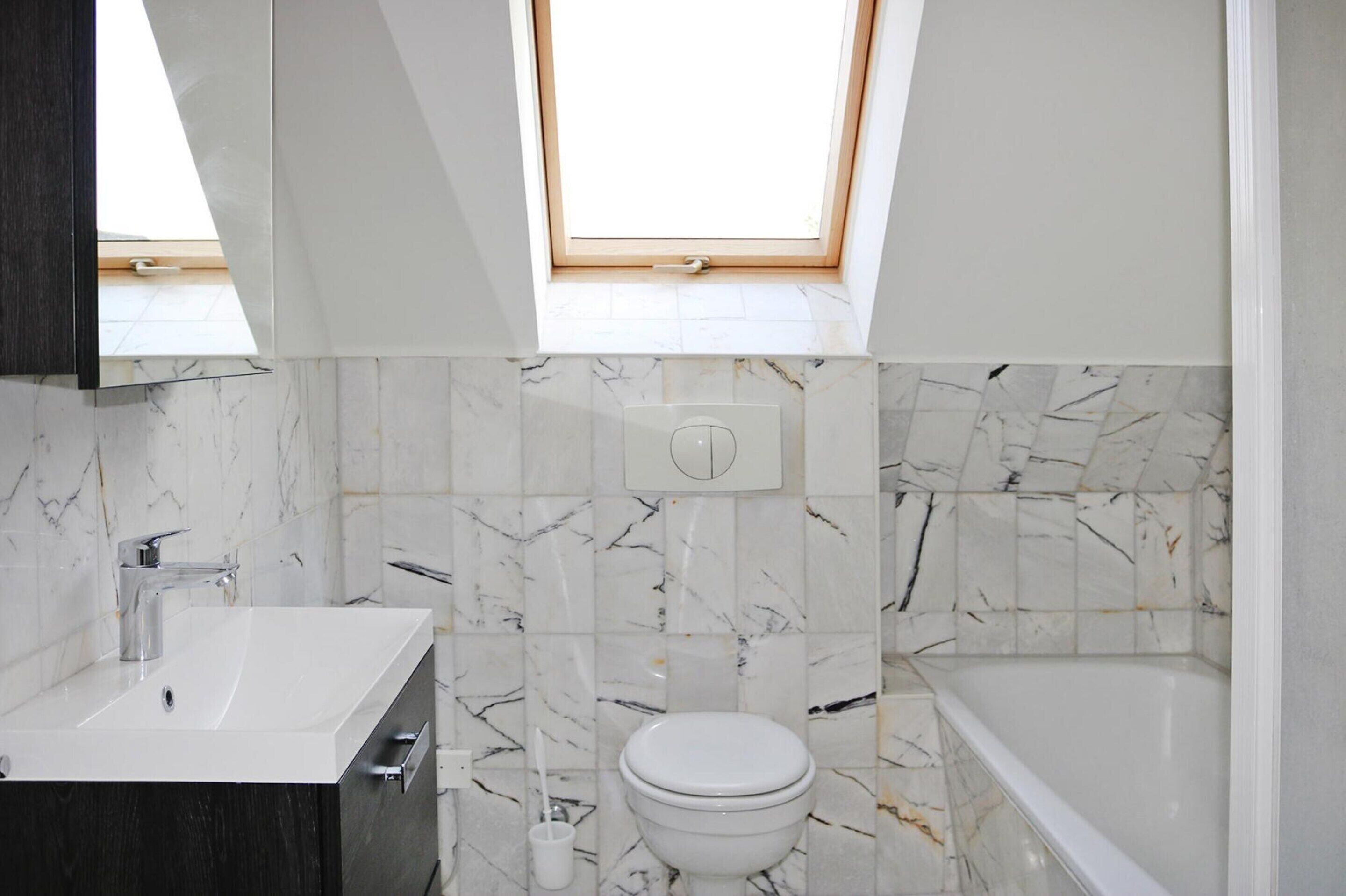 A modern bathroom with a skylight, a white sink, a toilet, and a bathtub.