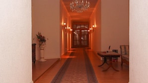 A hallway with a patterned carpet, a chandelier, wall sconces, and a dining area with a table and chairs. - Schlossurlaub Nahe Ostsee und Tressower See (Bobitz)