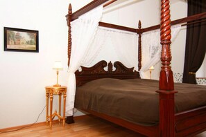 Un lit à baldaquin avec une structure en bois et des rideaux blancs, une table de chevet avec une lampe, et un tableau encadré accroché au mur.