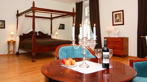 A bedroom with a four-poster bed, a dining table with fruit and wine, and a chandelier. - Schlossurlaub Nahe Ostsee und Tressower See (Bobitz)