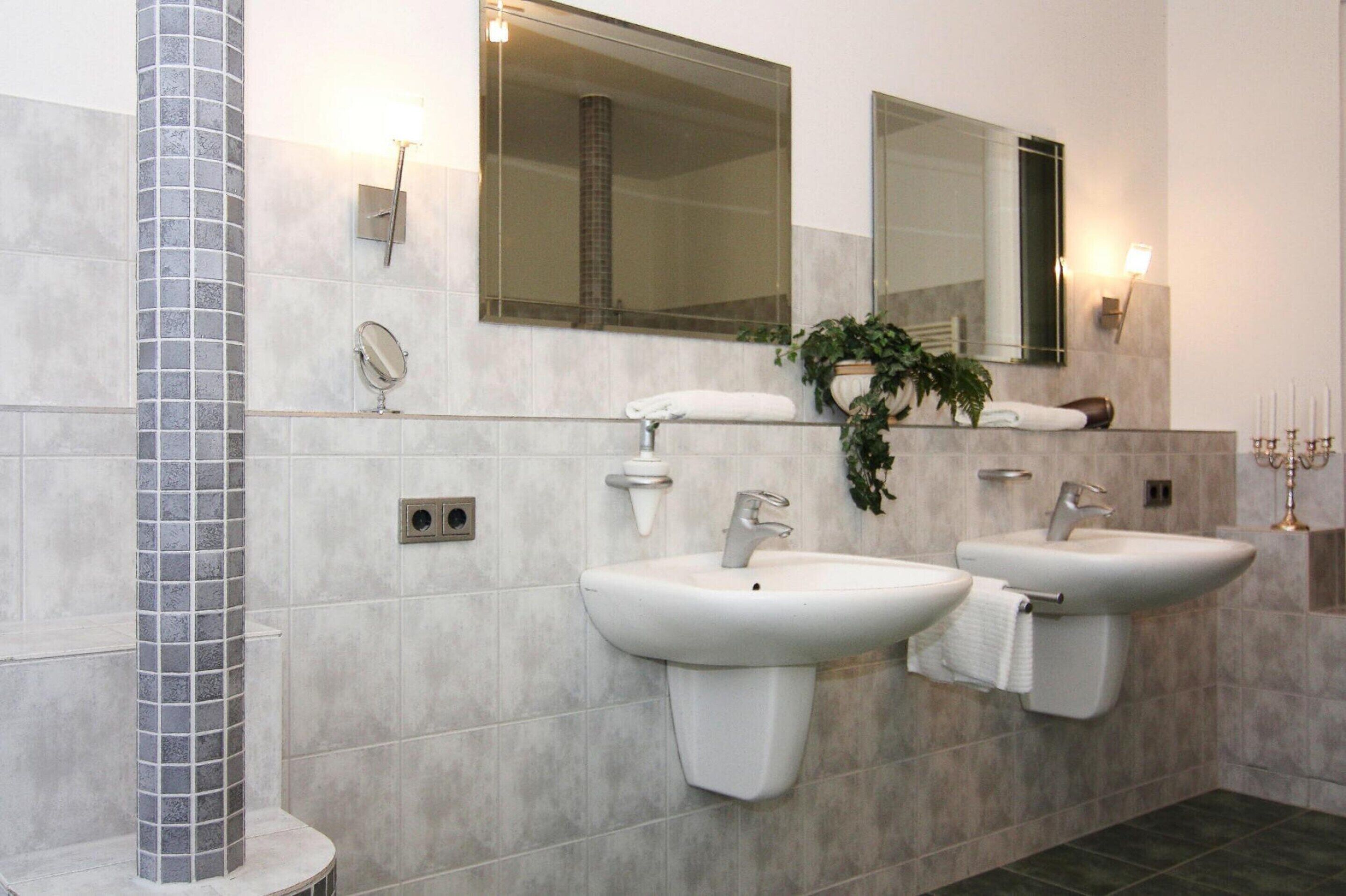 Une salle de bain moderne avec deux lavabos, un grand miroir et une colonne décorative.