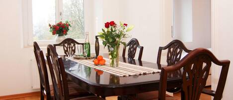A dining table with six chairs, a vase with flowers, and a bottle on the table.