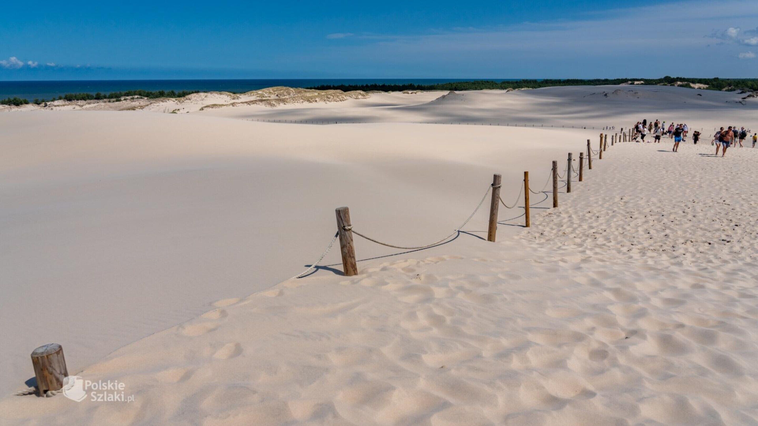 Una playa arenosa con una valla de madera y gente caminando.