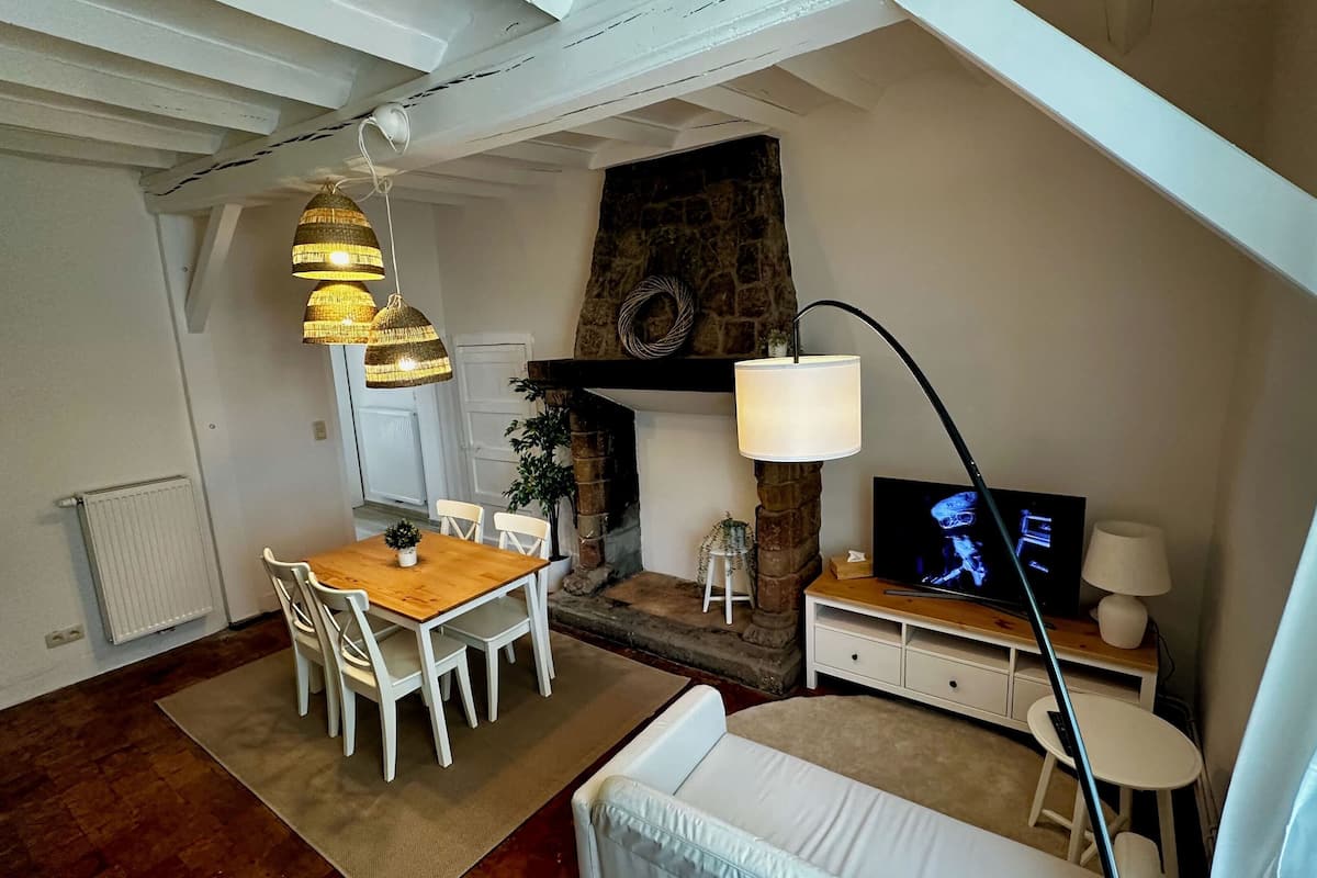 A cozy living room with a fireplace, a dining area with a wooden table and white chairs, and a TV on a wooden stand.