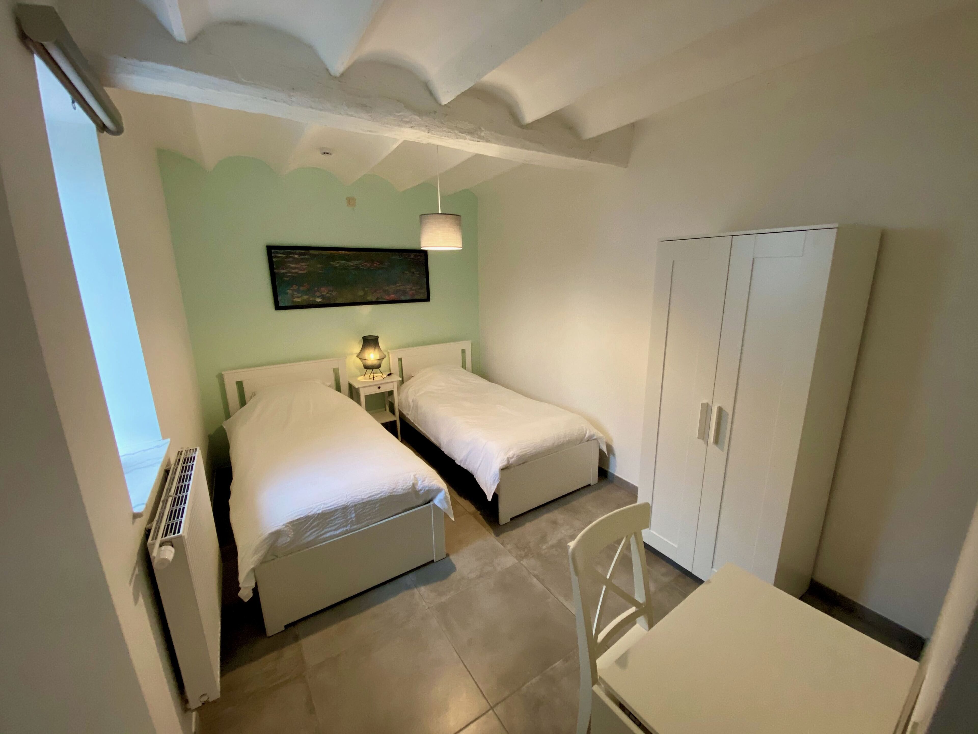 Une chambre avec deux lits, une table, une chaise, une armoire et un tableau au mur.