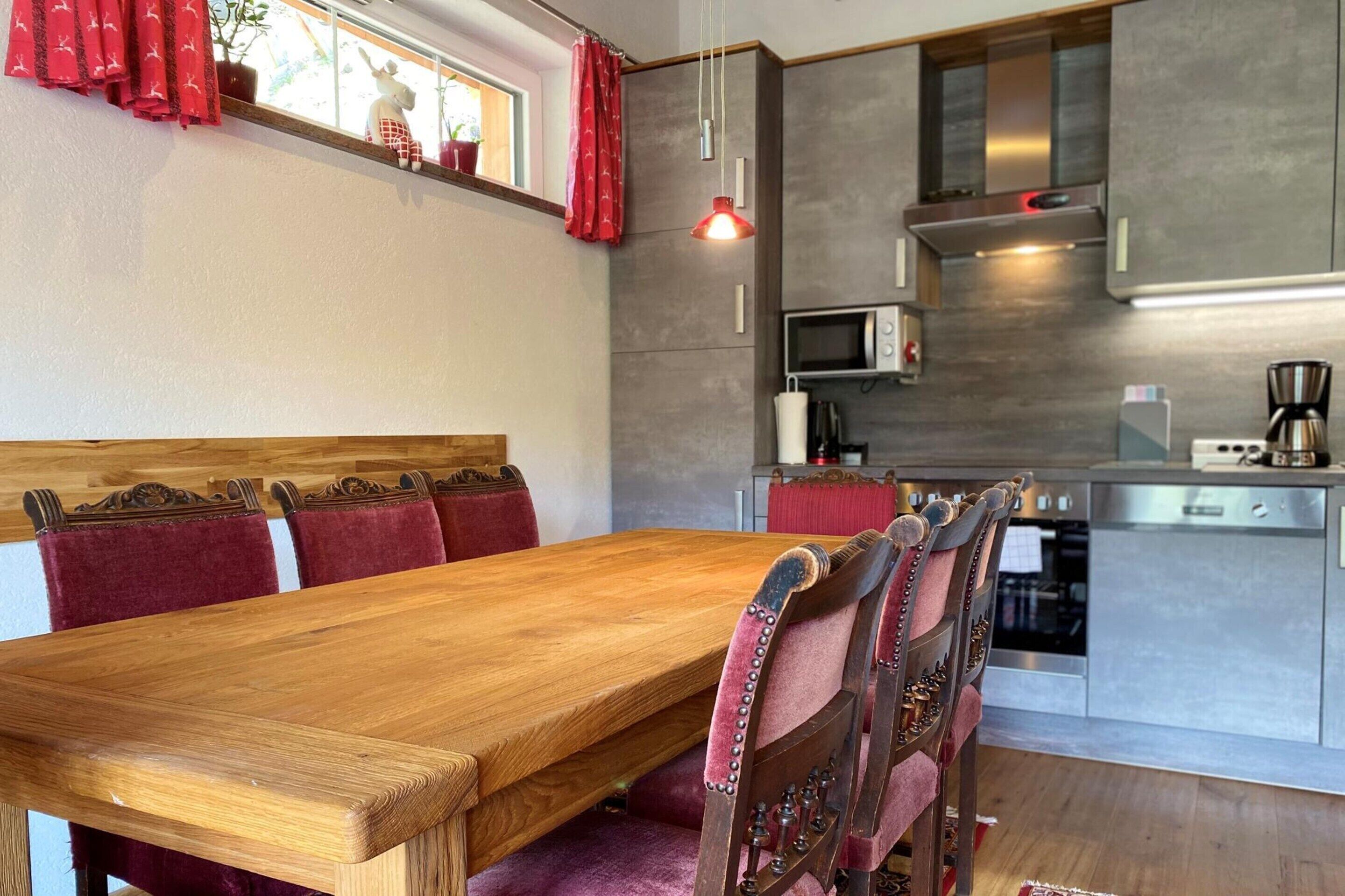 A modern kitchen with a wooden dining table and red upholstered chairs.