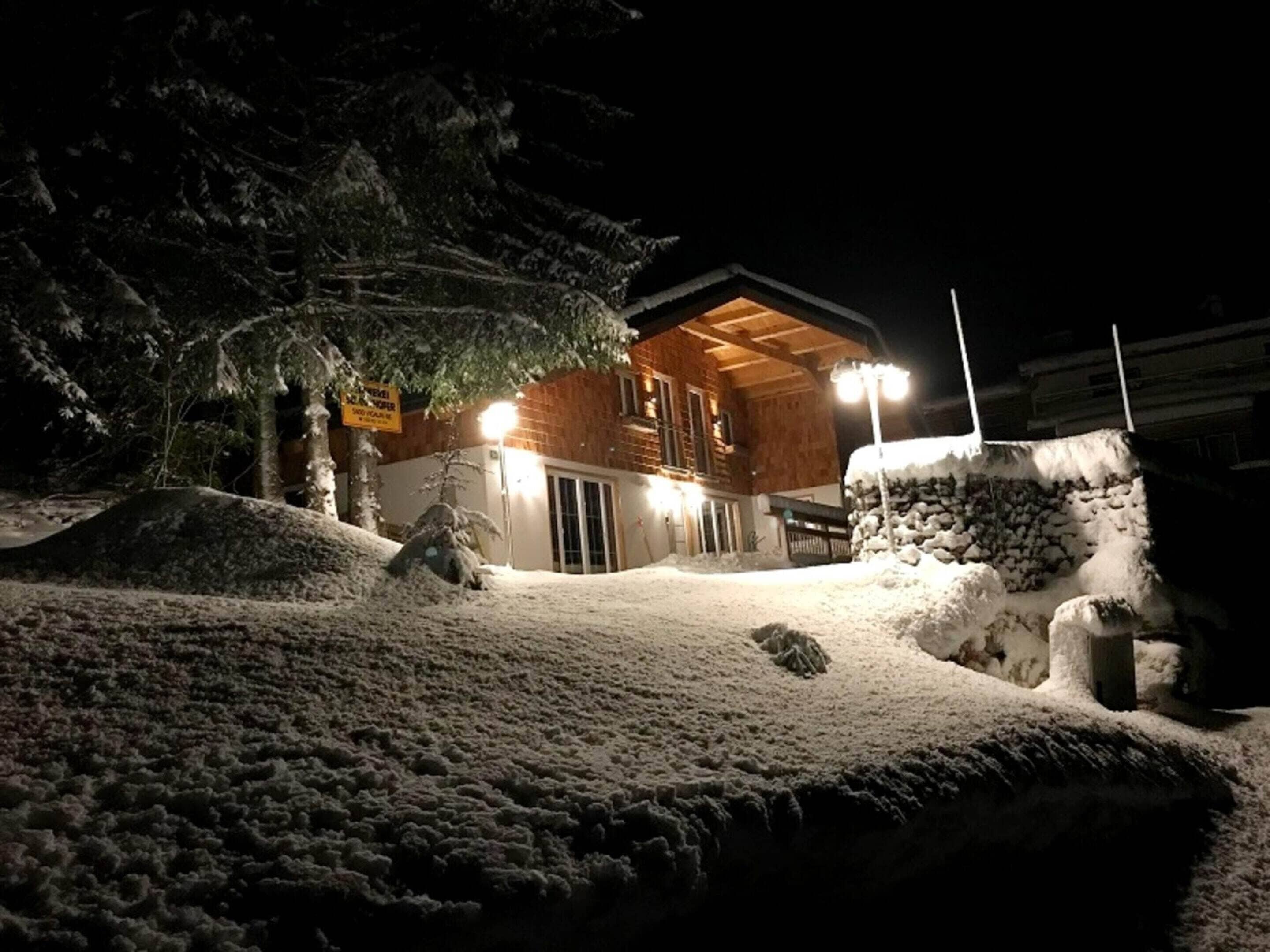 Een met sneeuw bedekt gebouw met een houten gevel, een verlichte ingang en een sneeuwduin ervoor.