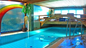 An indoor swimming pool with a wooden deck, a potted plant, and a sign in German.