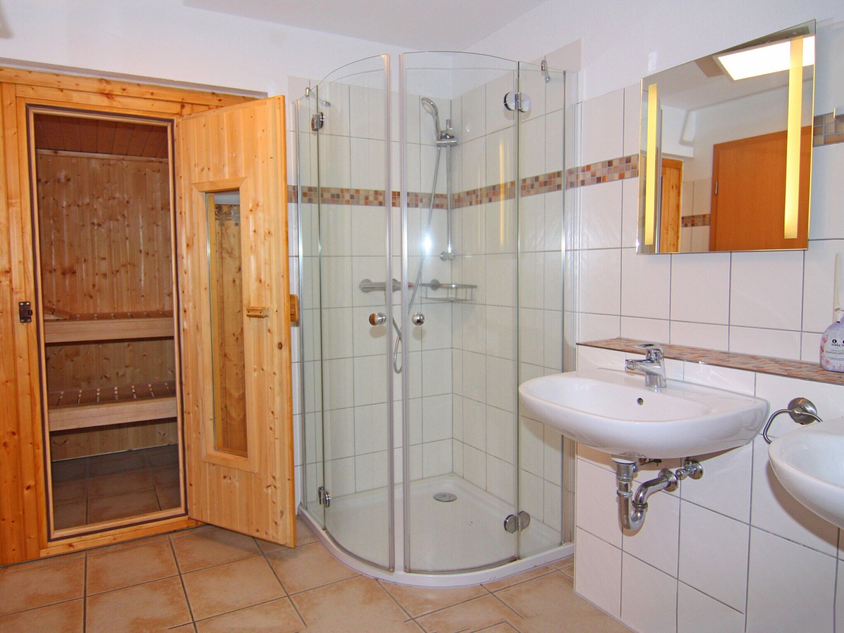 Ein Badezimmer mit Duschkabine aus Glas, Holztür, weißem Waschbecken und Spiegel.