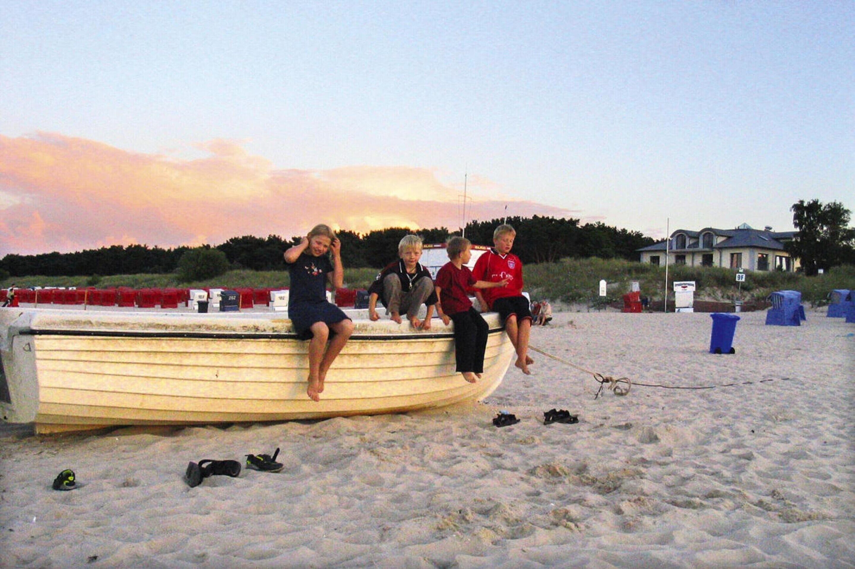A group of people sitting on a boat on a sandy beach with a house in the background.