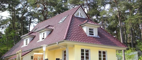 A two-story house with a red-tiled roof, a covered porch, and a small garden area.