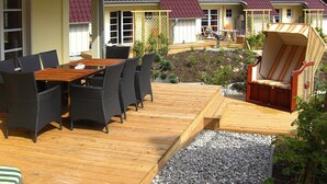 A wooden deck with a dining table and chairs, surrounded by a garden with a small pond and plants. - Doppelhaushalfte Ostseehaus I in Trassenheide (Trassenheide)