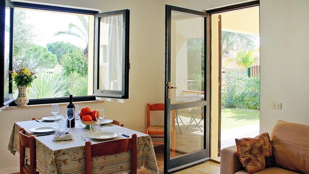 Un comedor con una mesa preparada para dos personas, un sofá y un ventanal corredero que da a un jardín.