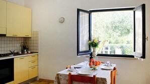 Una cocina con una mesa de comedor preparada para dos personas, una ventana con un persiano abierto y vista a la vegetación exterior.