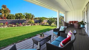 A covered patio area with wicker furniture, a grassy lawn, and a view of the surrounding landscape. - koolkondo 2606 Halalu Main house (Koloa)