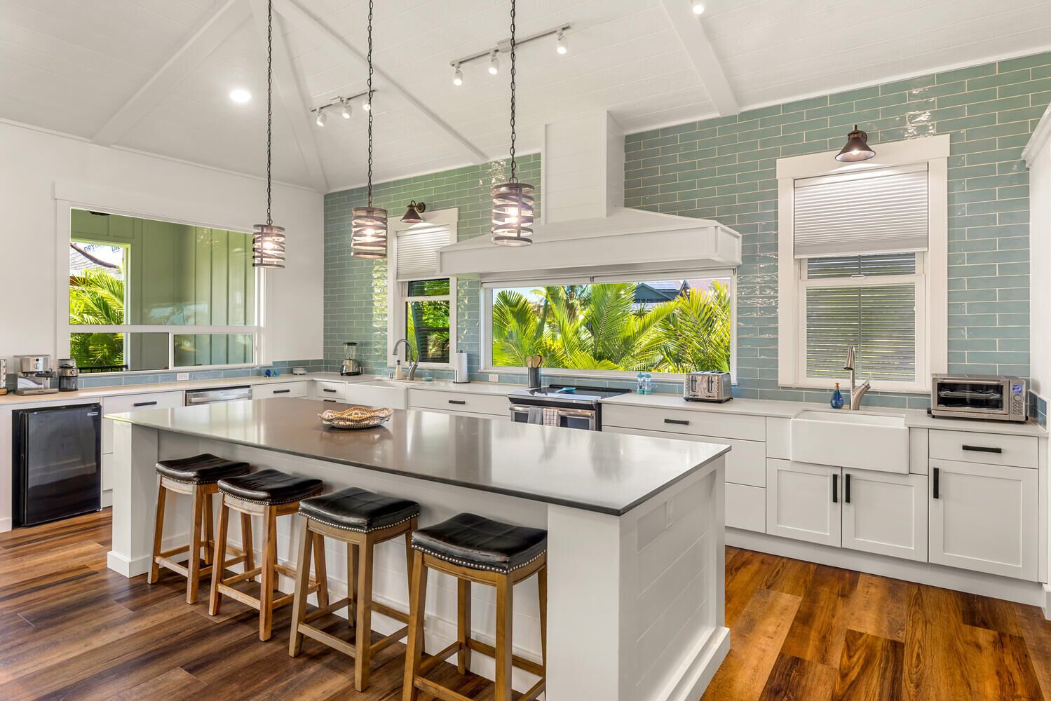 A modern kitchen with a large island, bar stools, and a view of greenery outside.