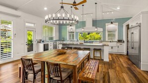 A modern kitchen with a central island, wooden flooring, and a view of greenery outside. - koolkondo 2606 Halalu Main house (Koloa)