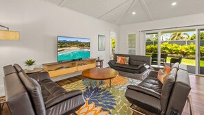 A modern living room with a large flat-screen TV, leather sofas, a wooden coffee table, and a colorful rug. - koolkondo 2606 Halalu Main house (Koloa)