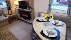 A cozy living area with a fireplace, a dining table set for four, and a sofa. - Cosy Hottub Caravan Retreat in Lincolnshire (Lincoln)