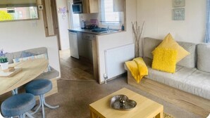 A compact living space with a kitchenette, a dining area with stools, a sofa with a yellow pillow, and a small table with a decorative item. - Cosy Hottub Caravan Retreat in Lincolnshire (Lincoln)