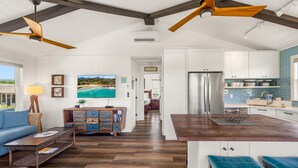 A spacious living room with a wooden ceiling fan, a blue sofa, a wooden coffee table, and a TV mounted on the wall. - koolkondo 2606 Halalu Guest house (Koloa)