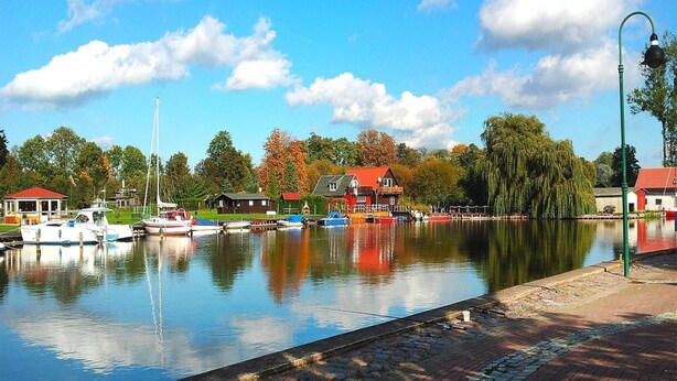 En rolig flod med fortøjede både, en bro og bygninger med røde tage langs flodbredden.