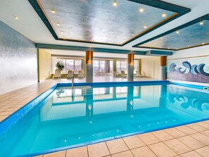 A large indoor swimming pool with clear blue water, surrounded by lounge chairs and a view of mountains through large windows. - Chalet on Zettersfeld With Dolomite Views (Thurn)