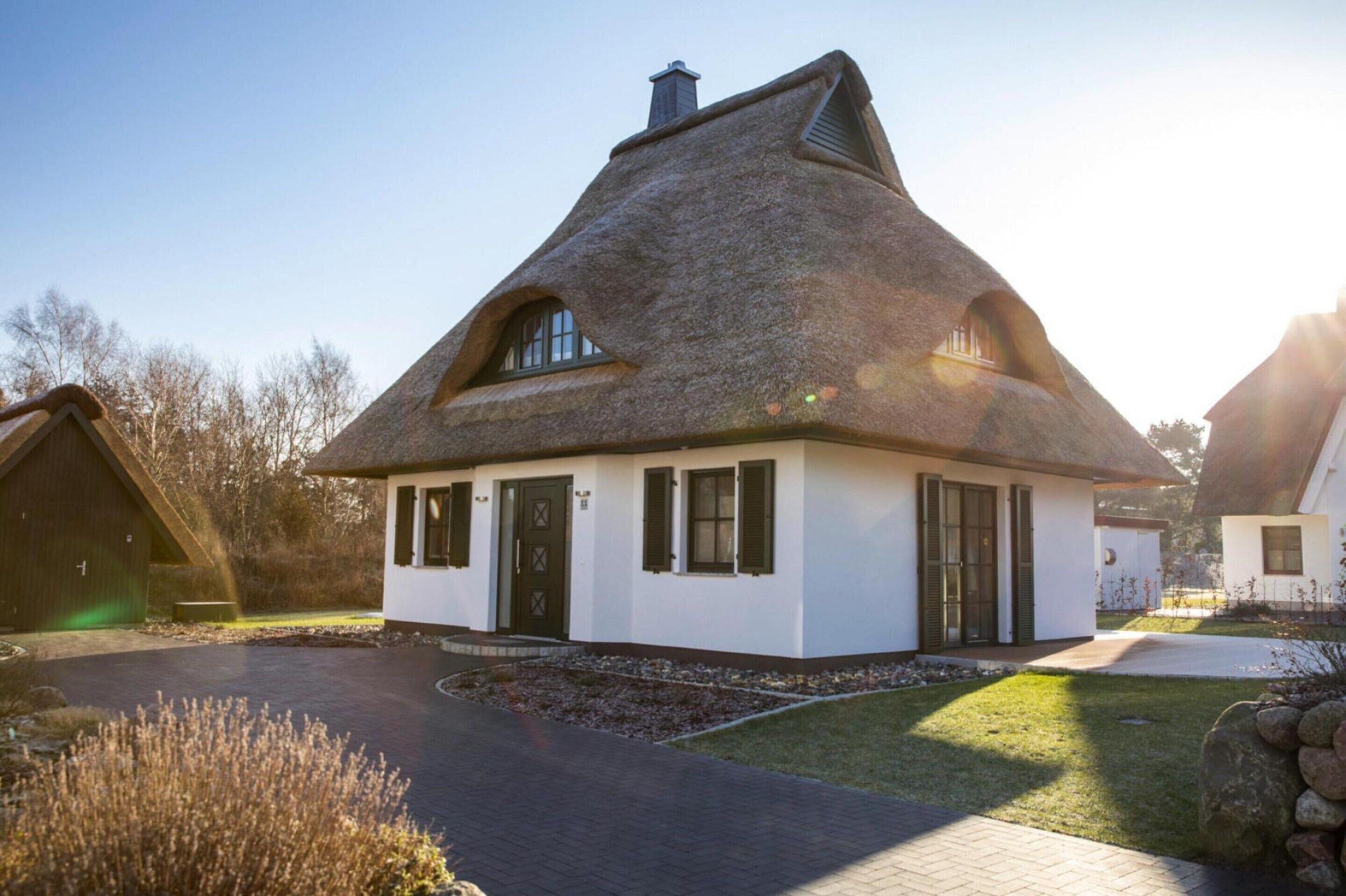 Une maison traditionnelle avec un toit de chaume, des murs blancs et un petit porche à l’avant.